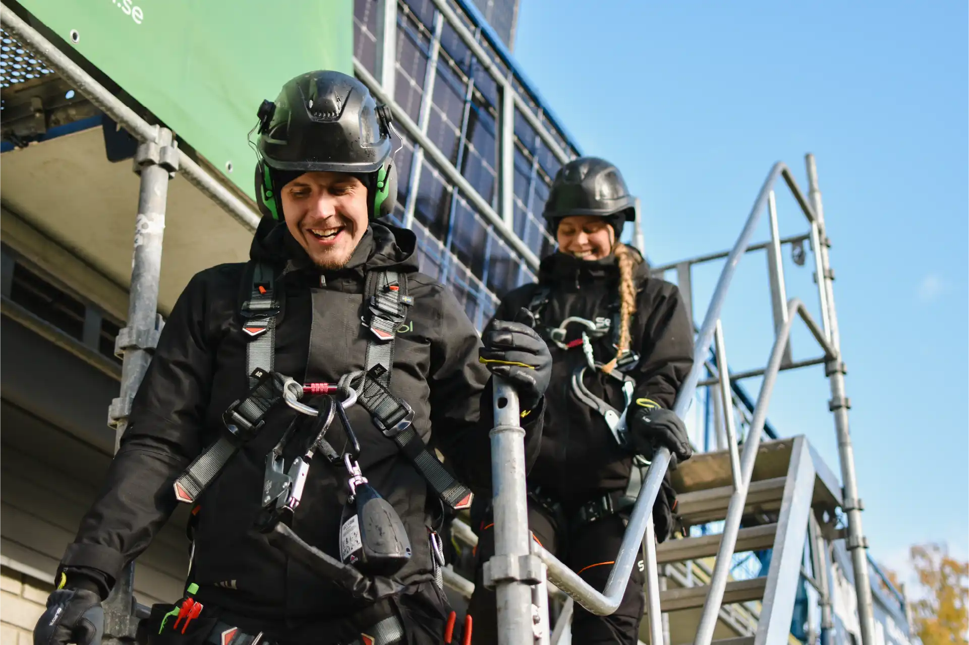 Två solcellsmontörer tar sig ner från taket via byggställning vid solcellsmontage